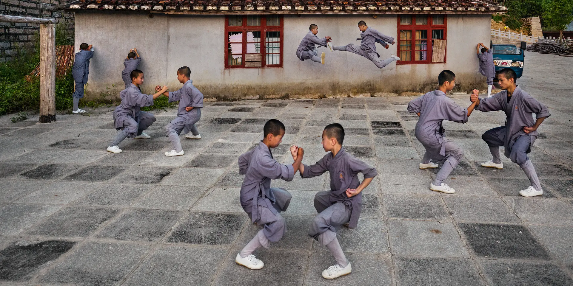 Shaolin monks practise martial arts in the courtyard in front of a traditional building